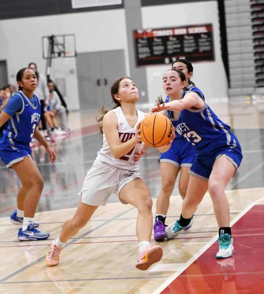 Young female basketball players competing in a game indoors.