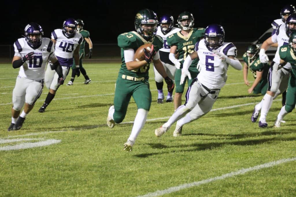 Running back in green uniform with football, evading defenders on the field.