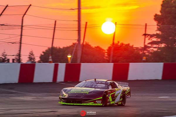Race car speeding on Madera Speedway track during sunset.
