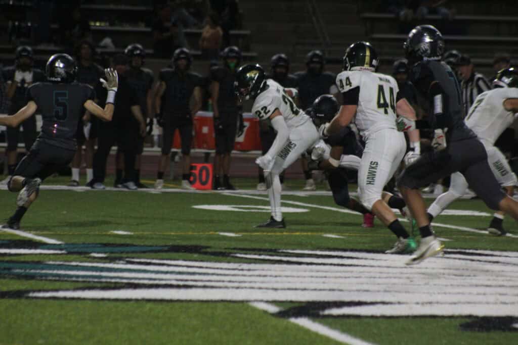 High school football game with players running on the field at night.
