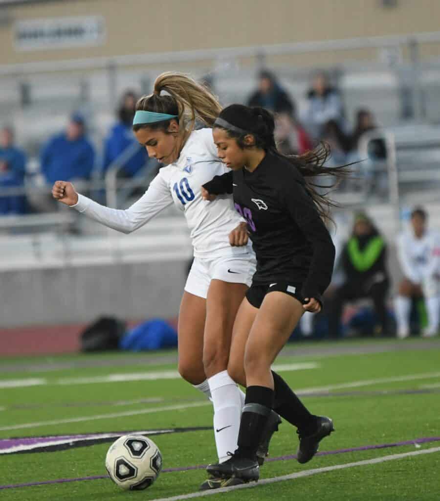 Two female soccer players battling for control of the ball during a match.
