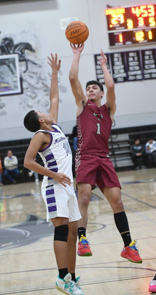 Player in maroon jersey shooting over defender in a high school basketball game.