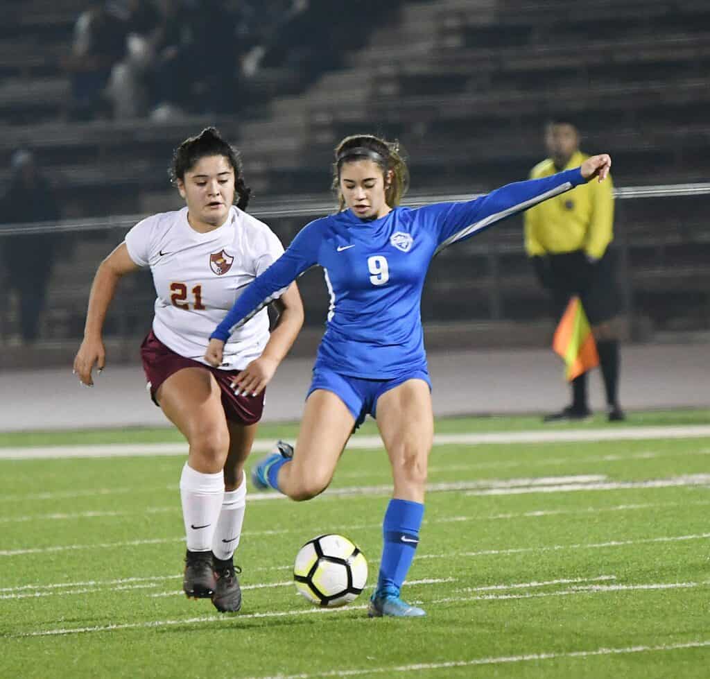 Female soccer player in blue scores a goal against Coyotes.