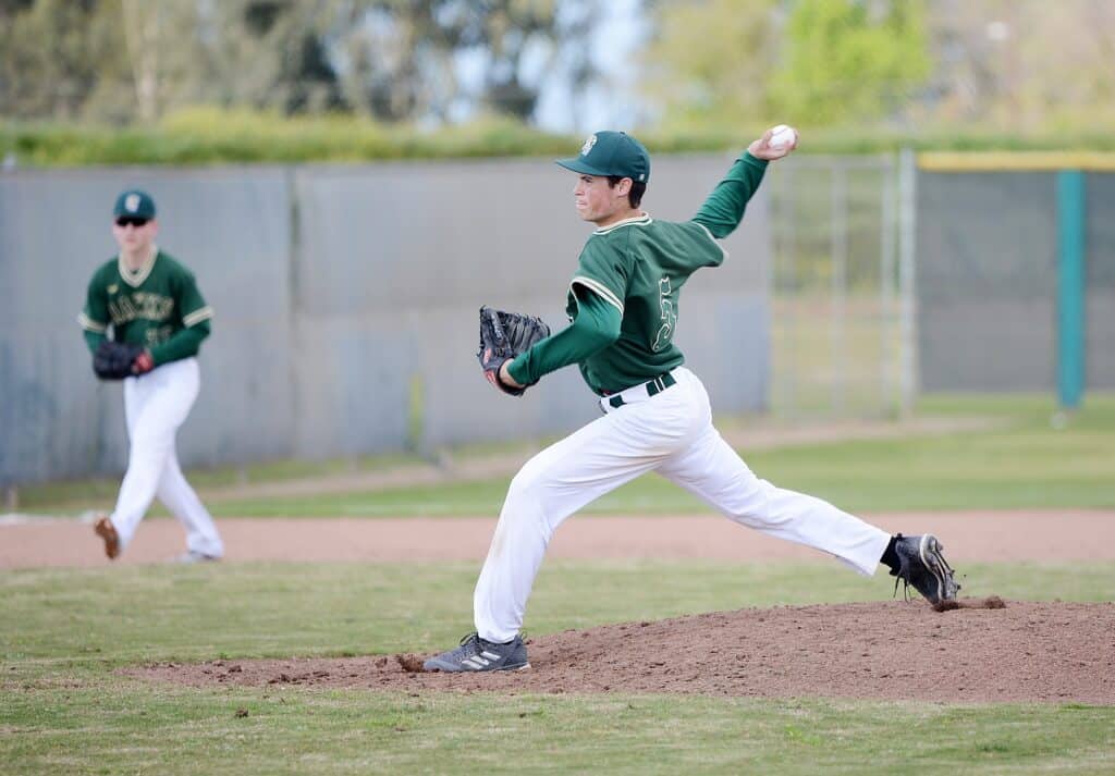 Young baseball pitcher in green uniform throwing a pitch on the field.