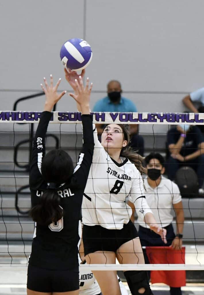 Female volleyball player spiking the ball during a match.