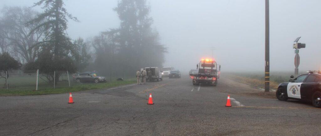 Accident scene at foggy intersection with police and emergency vehicles responding.