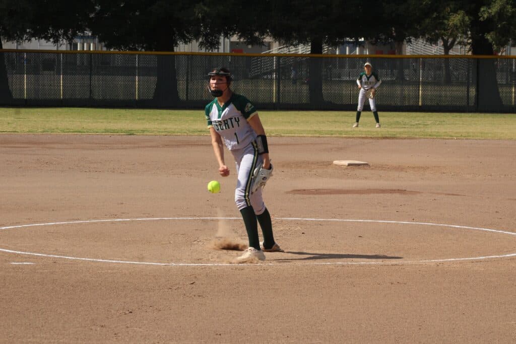 Female softball player pitching during a game on a sunny day.