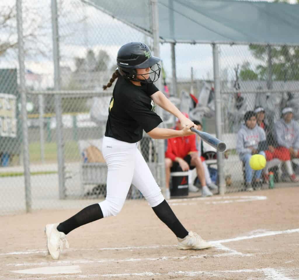 Young female softball player in black uniform swinging at a pitch.
