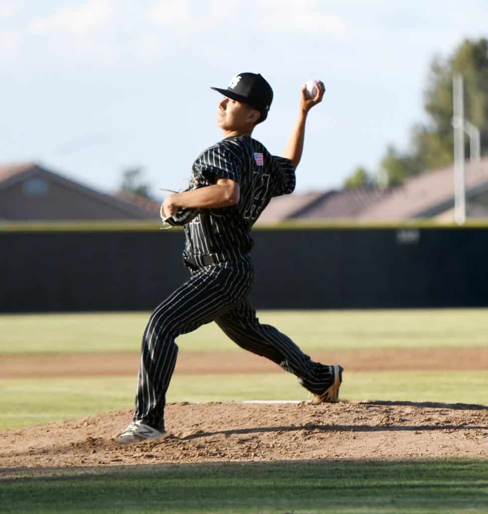 Young baseball pitcher in striped uniform on the mound during game.
