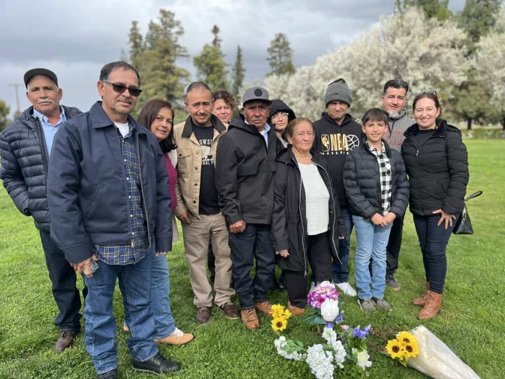 Family gathering at a park in Madera to honor a lost father, with flowers and somber expressions.