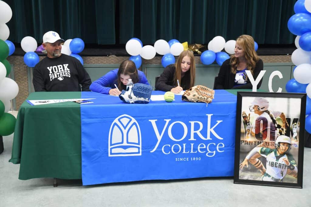 Young athletes signing with York College softball team at a school event.