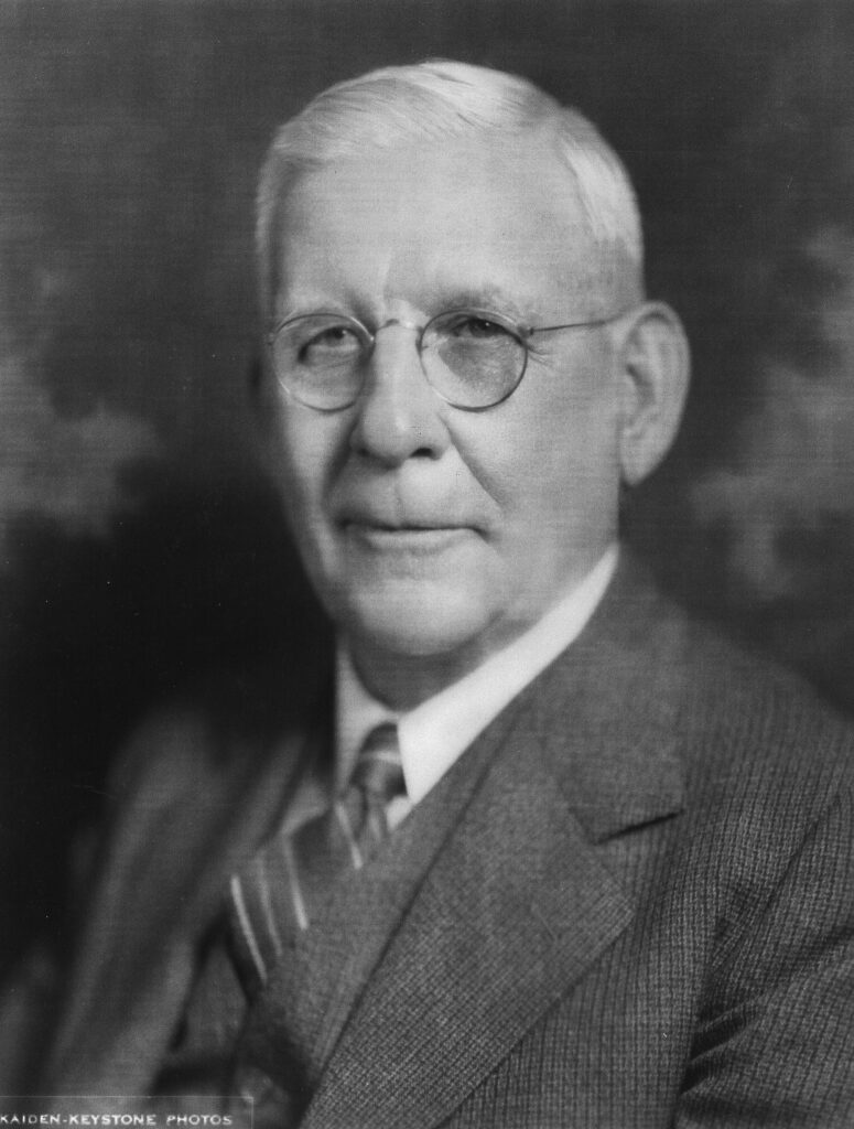 Black and white portrait of a distinguished man in glasses and suit.
