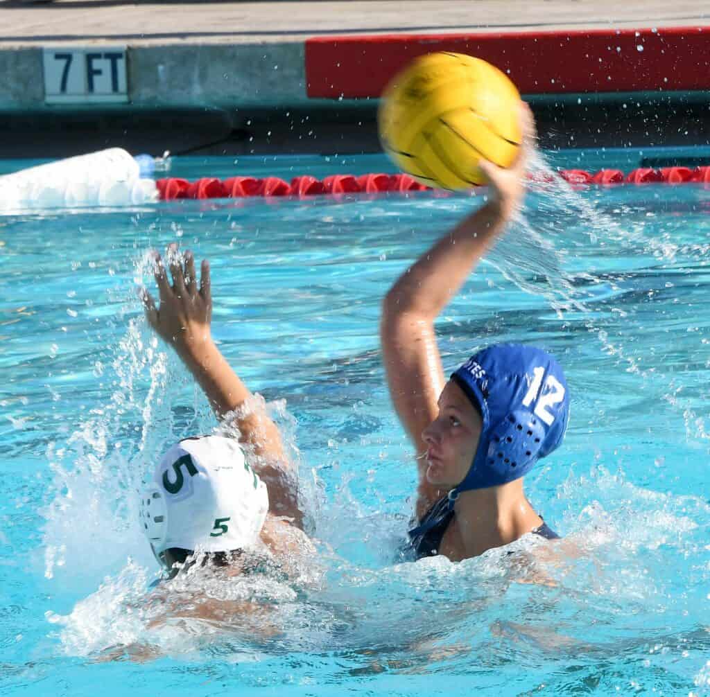 Female water polo player in blue cap preparing to throw the ball during a match.