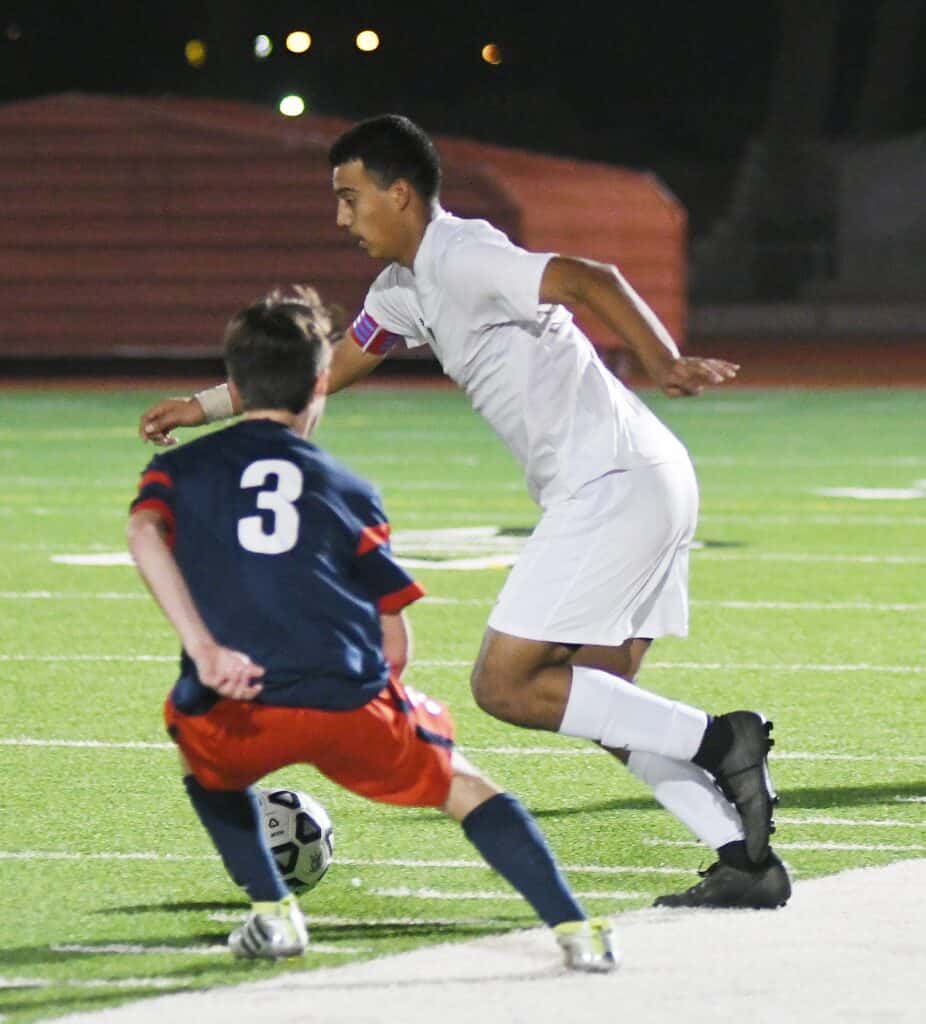 Two soccer players contest for the ball during a game at night.