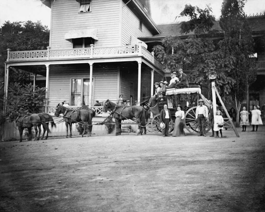 Historic black-and-white photo of a horse-drawn carriage in front of a house.
