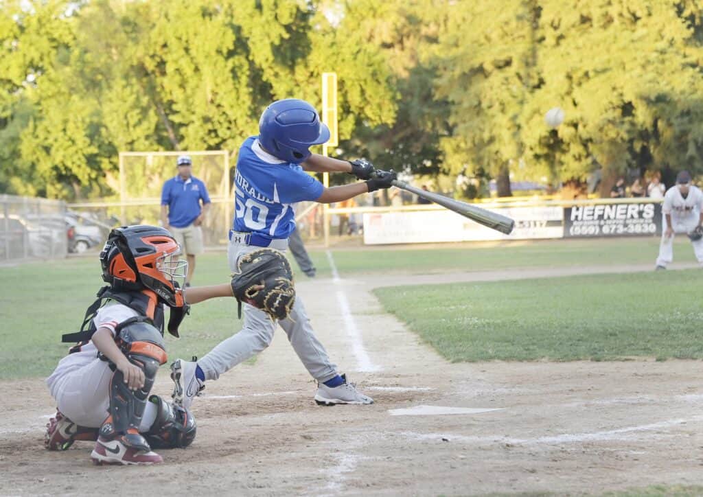 Young baseball player hits ball during game at Madera field.