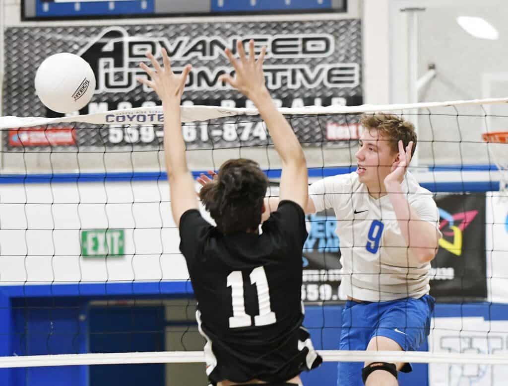 Senior volleyball player spikes the ball past opponent at the net.