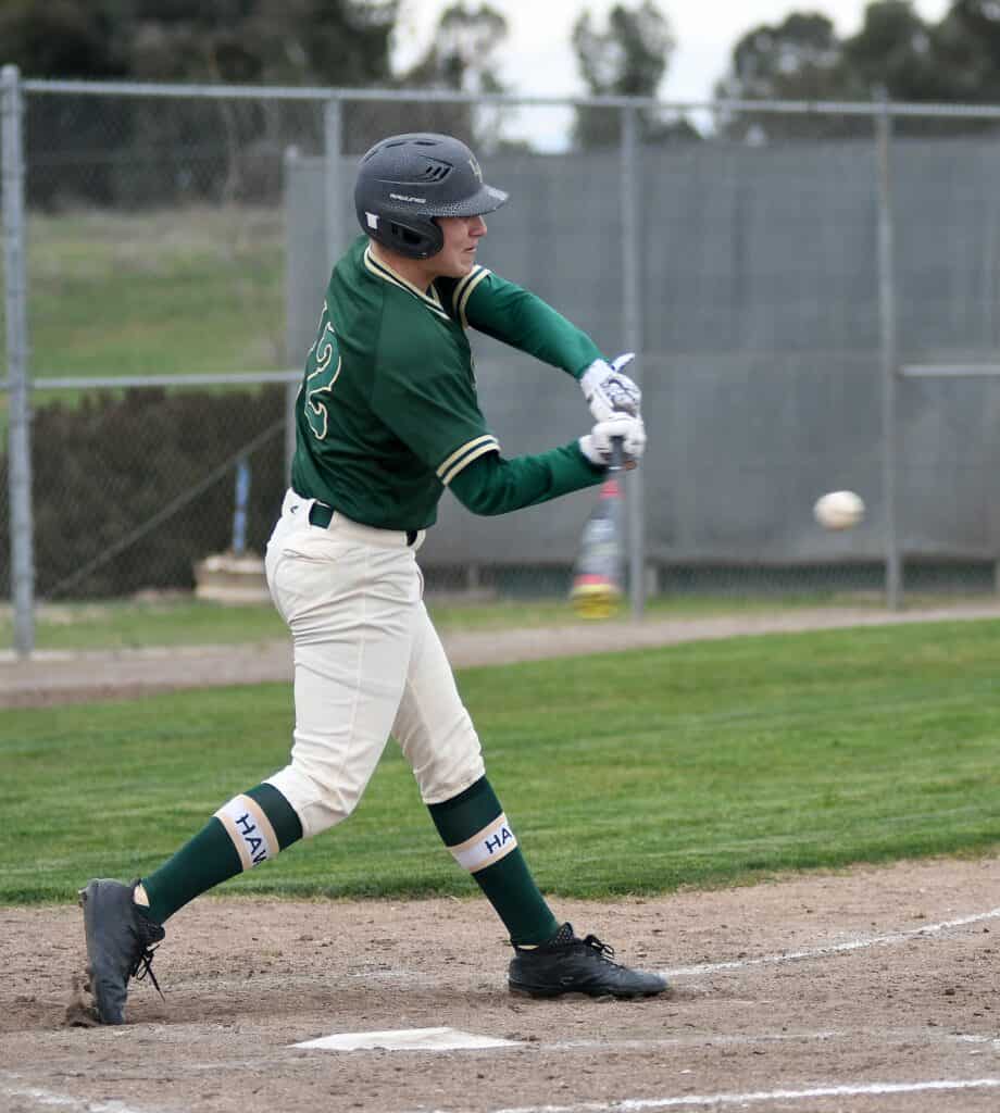 Young baseball player in green uniform swinging at a pitch during a game.