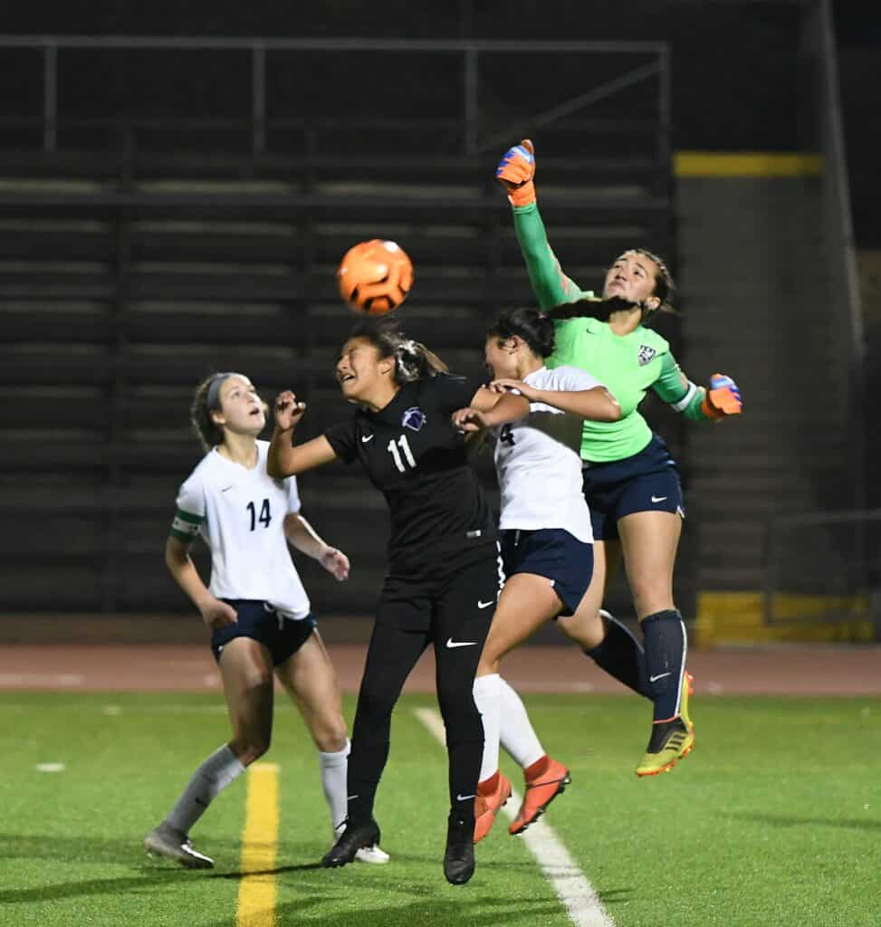 Girls soccer players competing for the ball during a match at night.