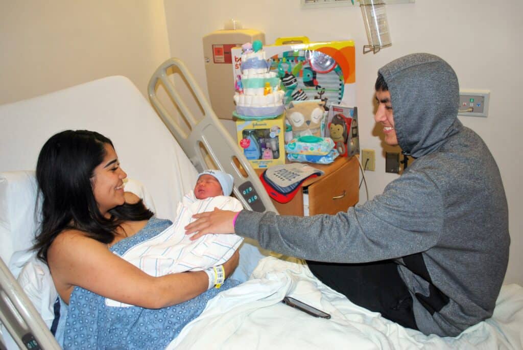 Newborn baby in hospital bed with mother and visitor.
