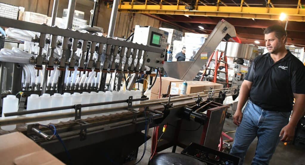 Man operating sanitizer filling machine at Riley’s Brewing for sanitizer production.