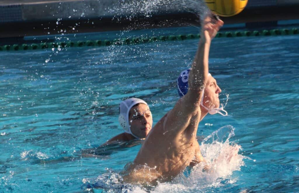 Water polo players competing in a match, focusing on a player reaching for the ball.