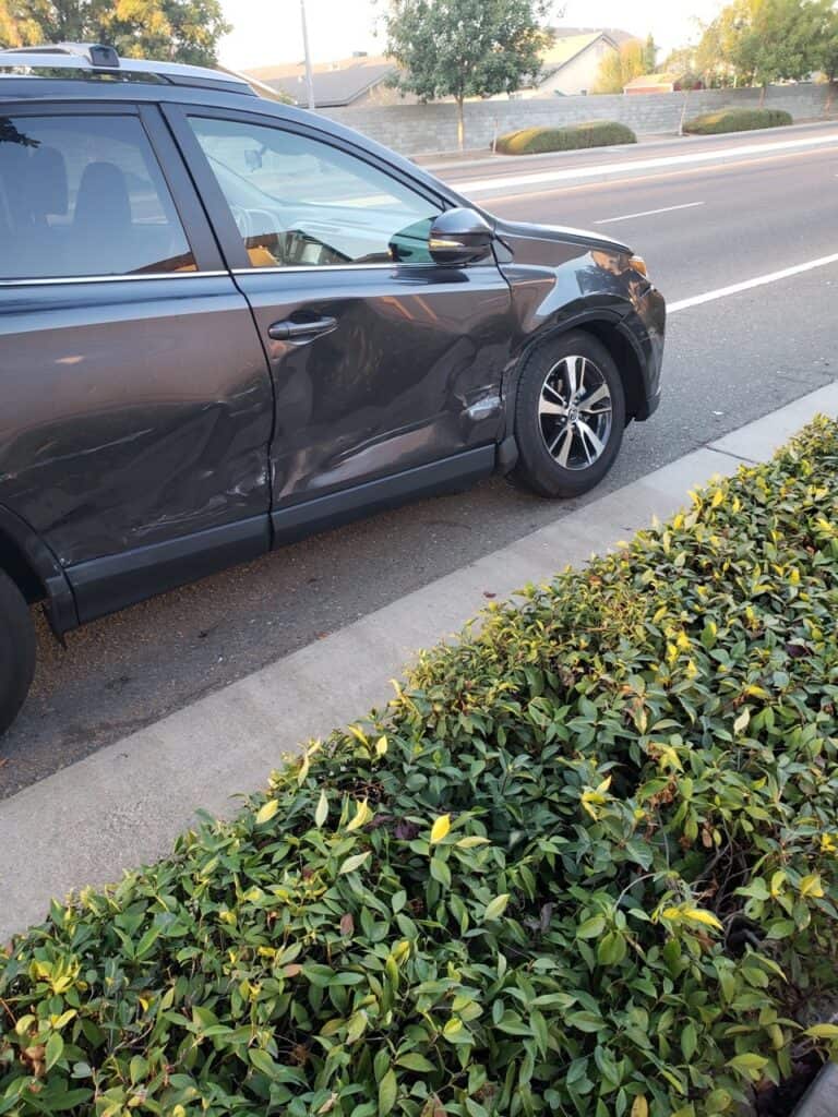 Damaged car parked near overgrown bushes, waiting for stoplight installation.