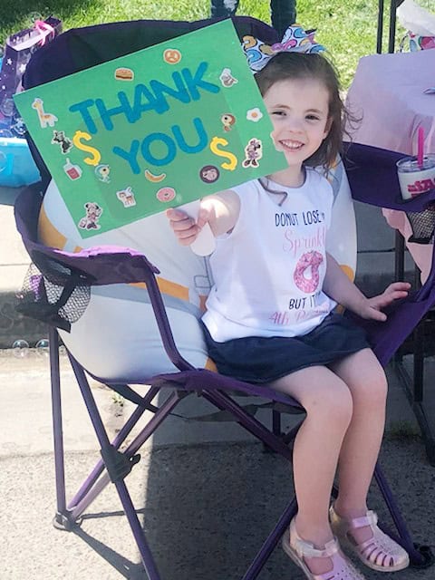 Child holding a colorful "Thank You" sign at donation event.