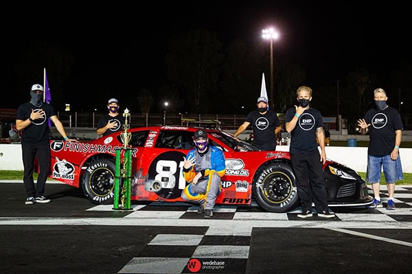 Race team celebrating victory with a red race car and trophy.