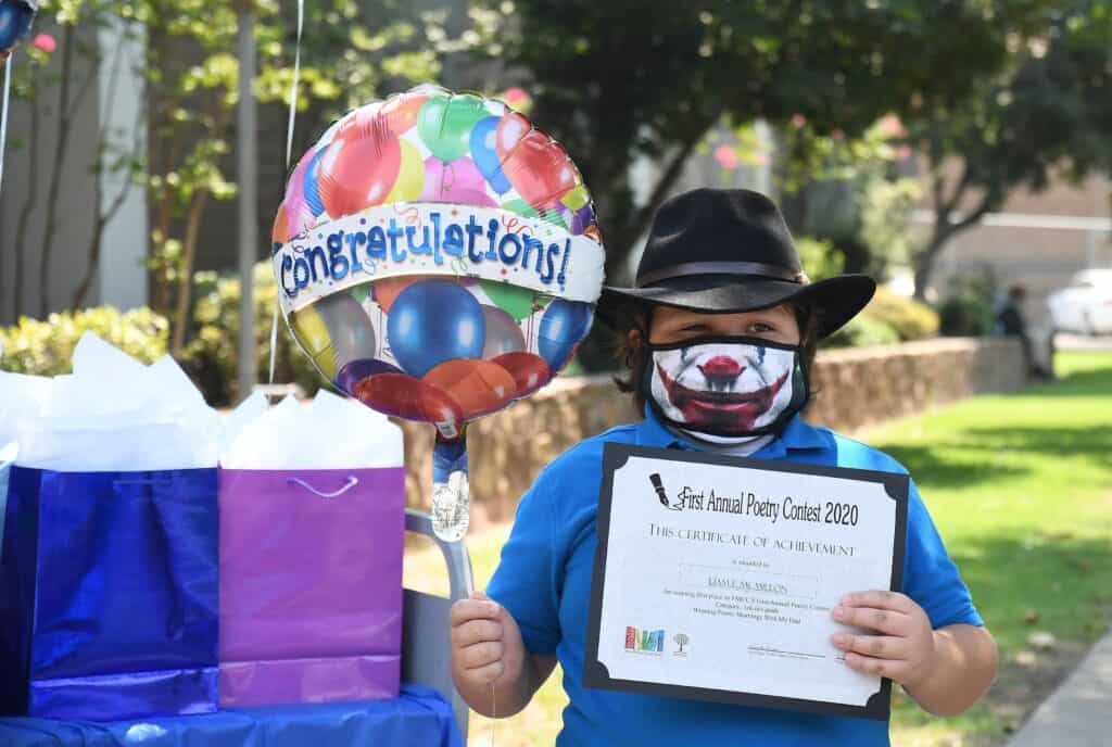 Poet holding a certificate and colorful balloon at Madera County event.