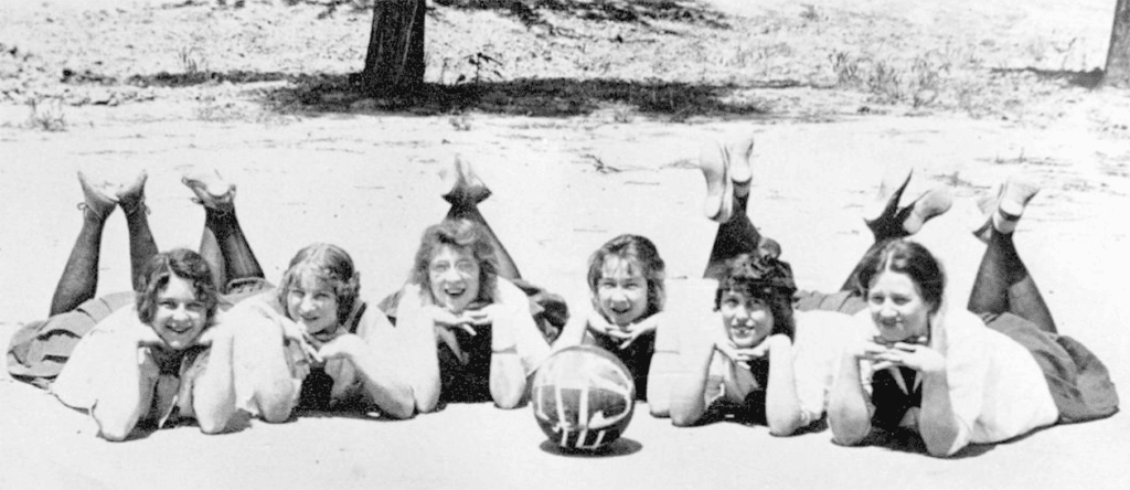 Young female athletes lying on the ground with a volleyball, reflecting a recent sports competition.