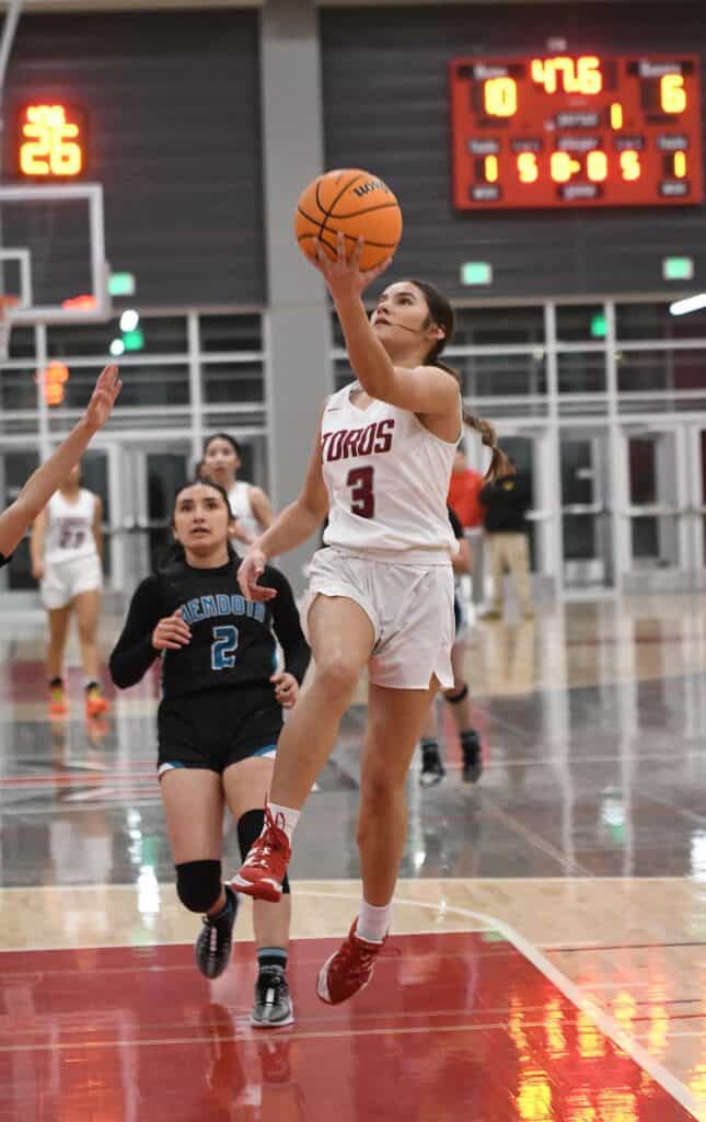 Female basketball player in Madera Toros uniform going for a shot during game.