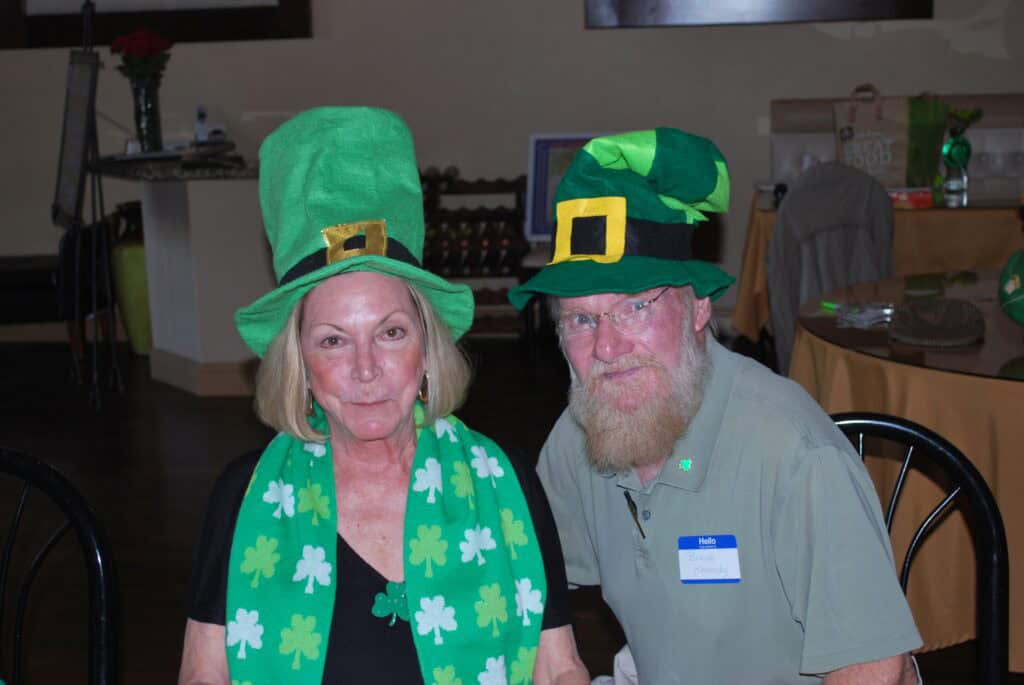 Two people wearing green hats and shamrock scarves at St. Patrick's Day event.