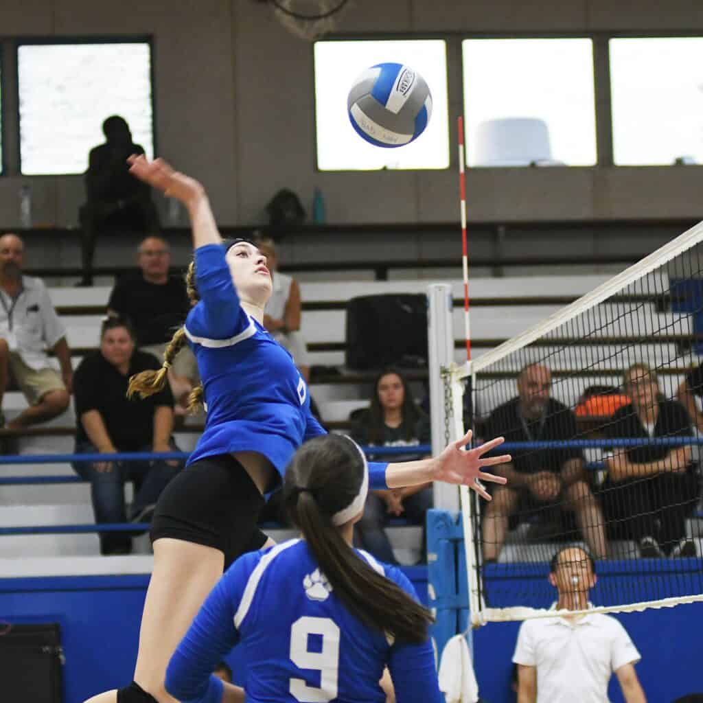 Female volleyball player spiking the ball during a match at the Madera gym.