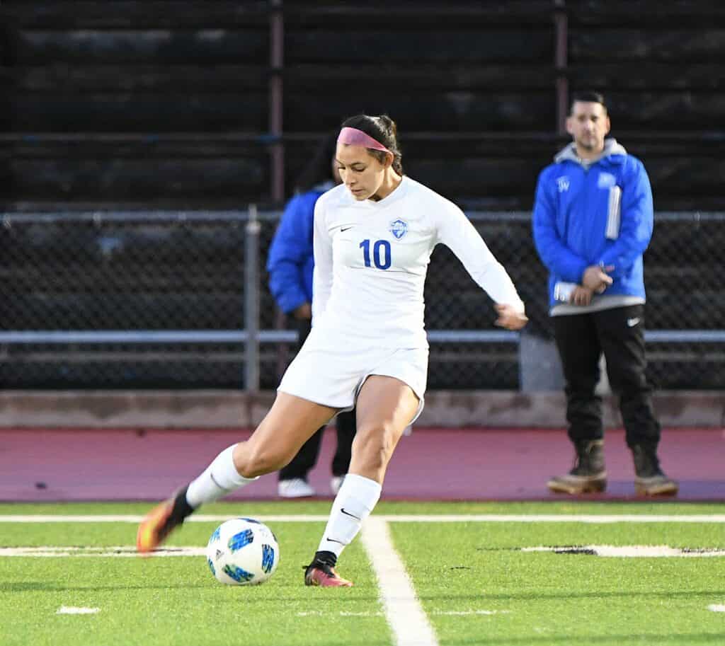 Soccer player wearing number 10 in white uniform kicks the ball during a match.