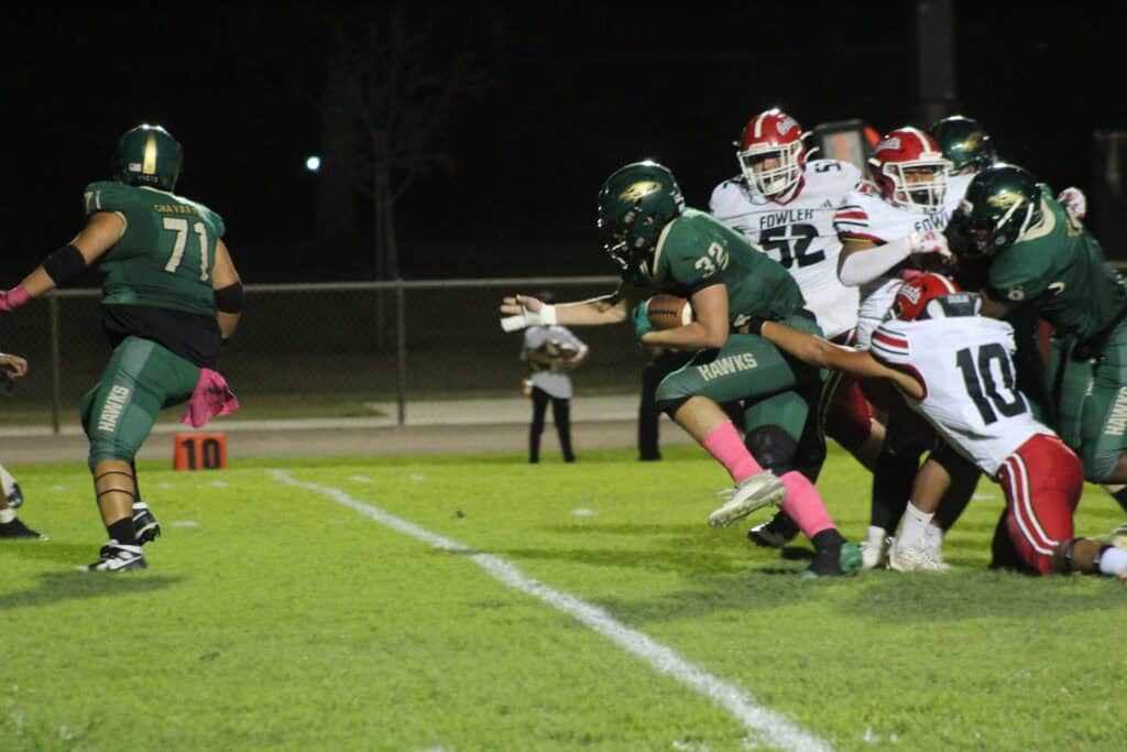 Madera Hawks football players in action during a game at night.