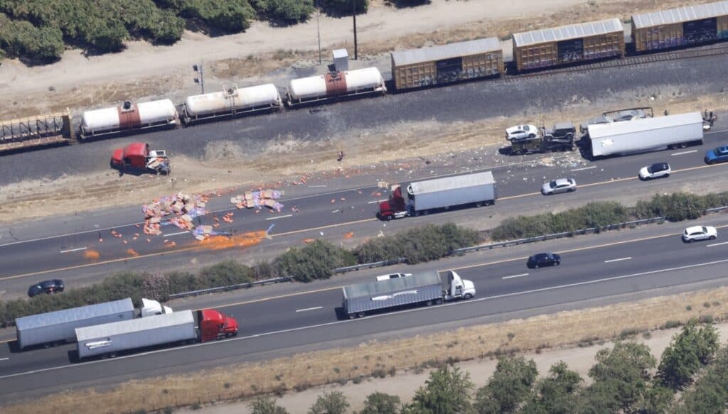 Accident on highway involving trucks and cars, debris scattered after crash. Emergency response ongo.