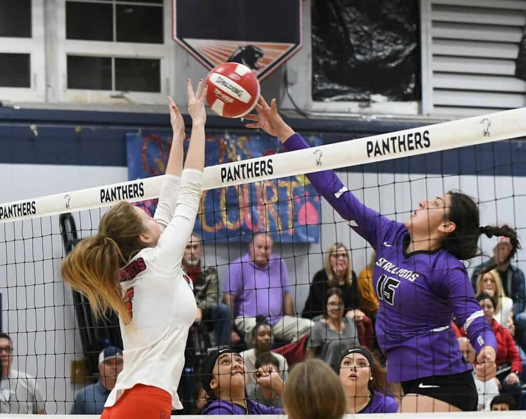 Girls' volleyball game at Memorial, with players jumping for the ball at the net.