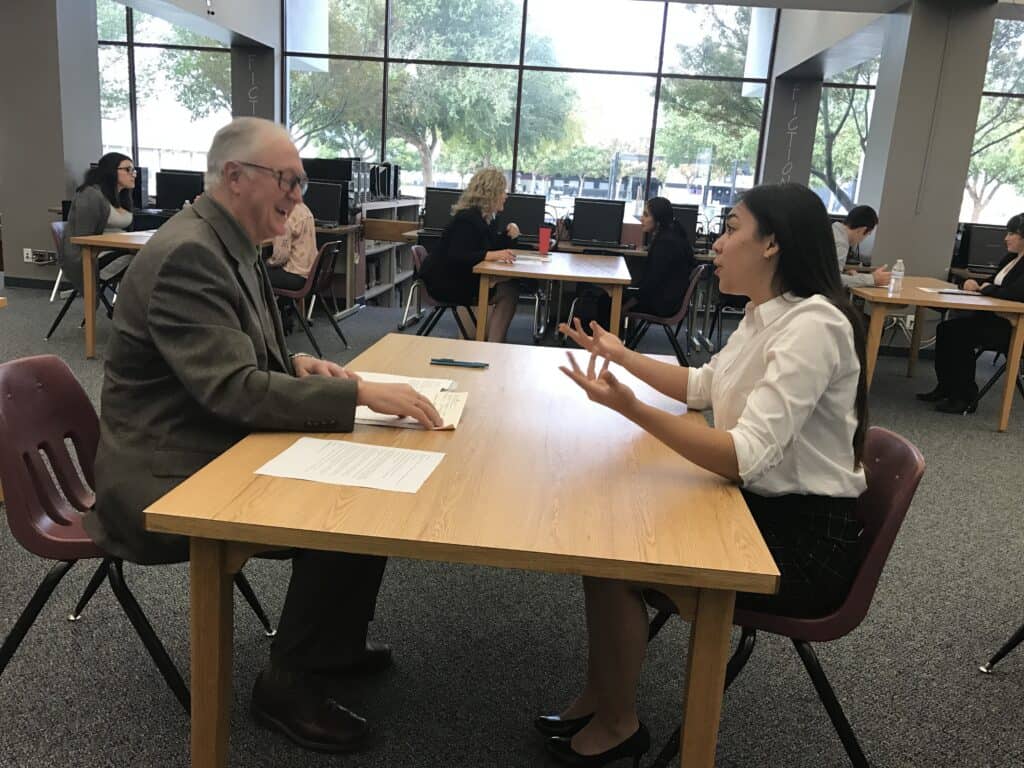 Senior and young adult engaging in a mock interview at a table.