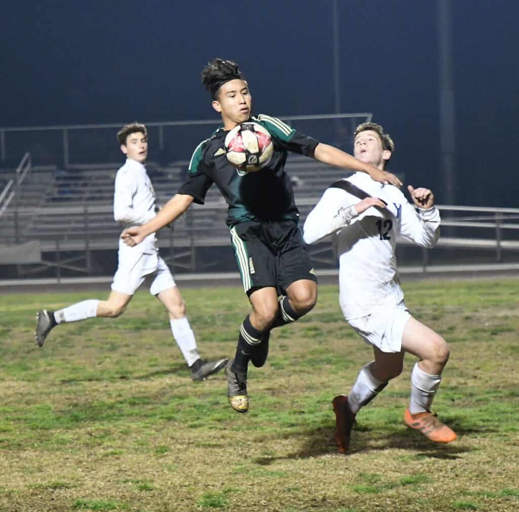 Young soccer players battling for the ball on a grassy field under stadium lights.