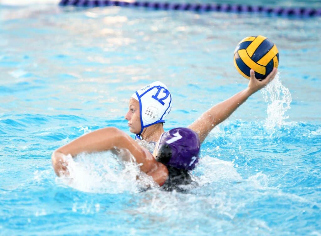 Female water polo player in action, holding a yellow and blue ball during a game.