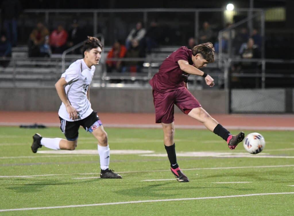Soccer players competing in a high school match at night.