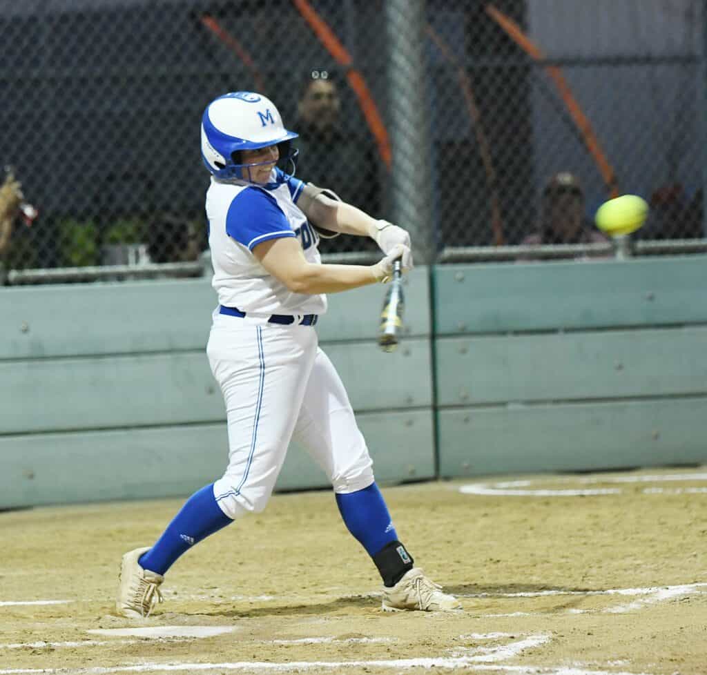 Female softball player in blue and white uniform swinging at pitch.