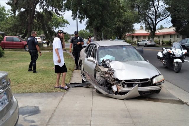 Accident scene showing a damaged silver car after colliding with a mailbox, with police officers and.