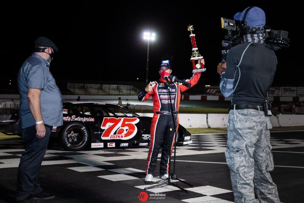Doss wins at Madera Speedway, holding trophy after a thrilling race finish.
