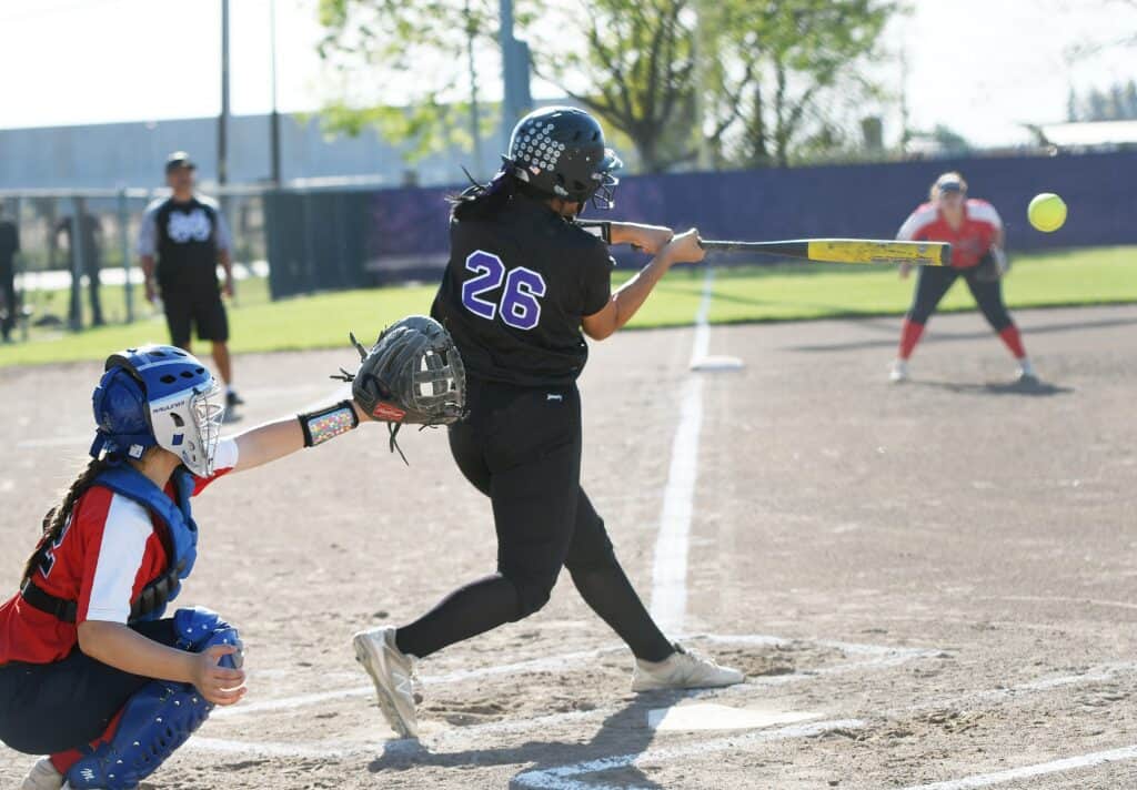 Female softball player swinging at pitch during Senior Night game.