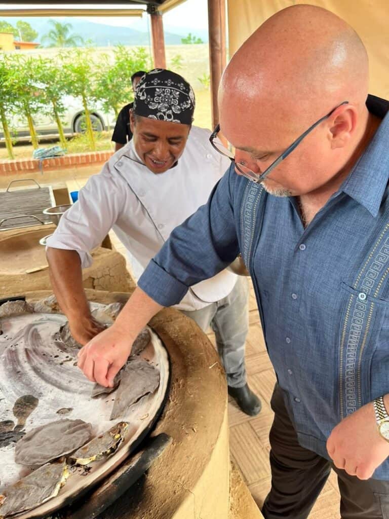 Oaxaca chef and visitor preparing traditional fish at a local culinary event.