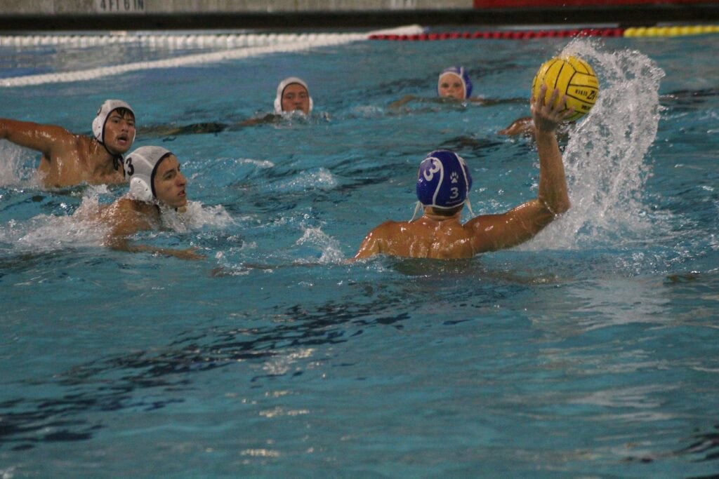 Water polo players competing in a match, focusing on player with ball.