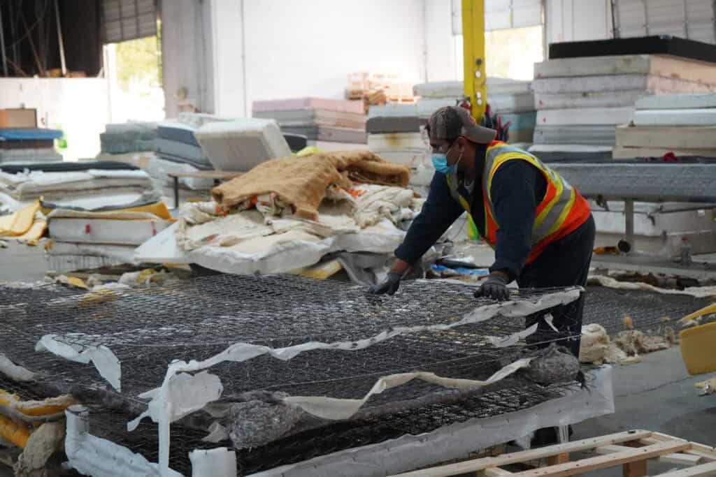 Worker recycling mattresses to reduce landfill waste and promote environmental sustainability.