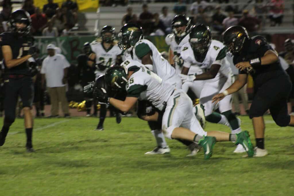 Madera football players tackling during a game at night.